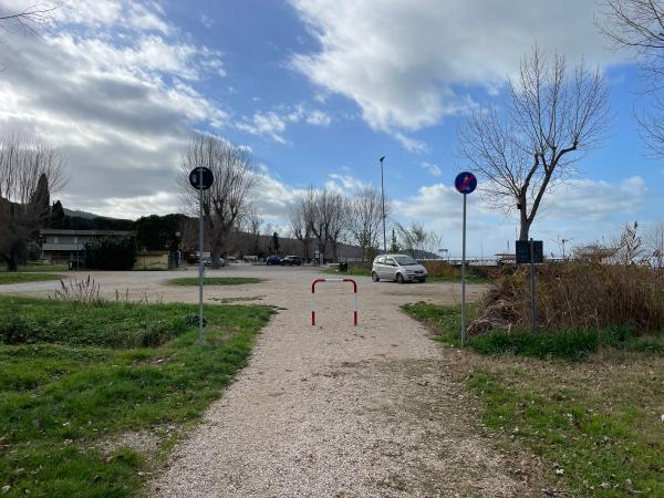 Section gravillonnée de la piste cyclable. Une barrière de sécurité la sépare d'un parking. A droite, un panneau de fin de piste cyclable.